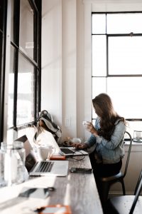 Young woman working at a computer and drinking a beverage in a cup.