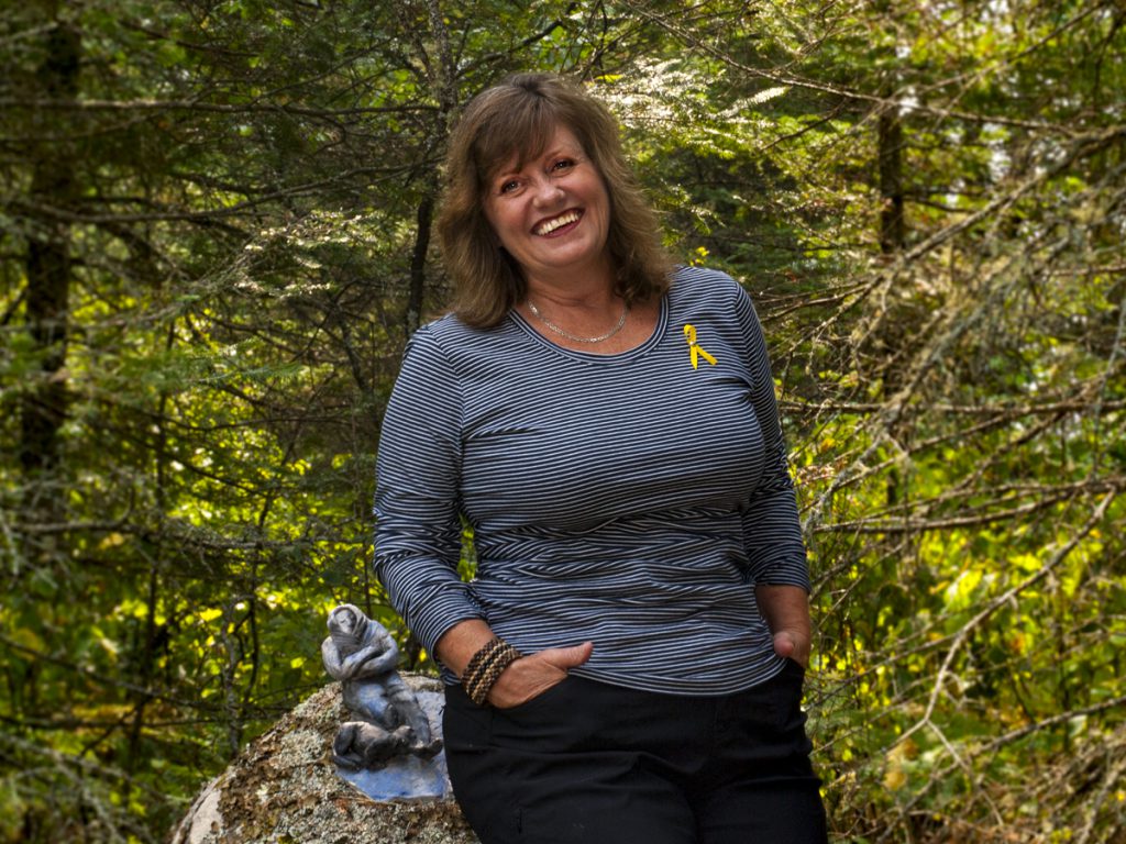 Leanne Fournier standing in the bush with a small sculpture by her side.