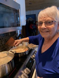 Older woman in blue shirt cooking perogies. 