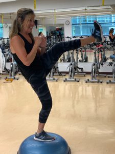 Woman on a bosu ball kicking forward. 