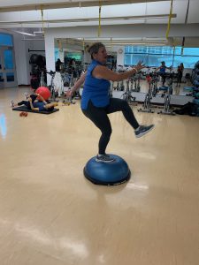 Woman on a bosu ball kicking forward looking strained. 
