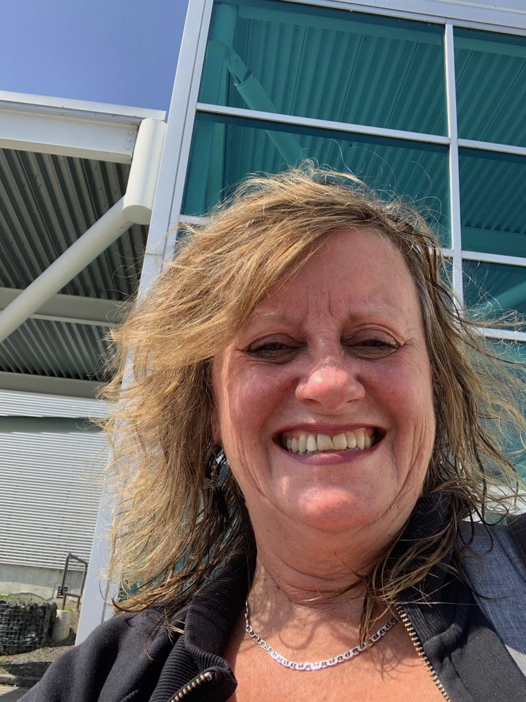 Leanne Fournier with wet hair smiling outside of the recreation centre where she has just completed a very tough fitness class. 

