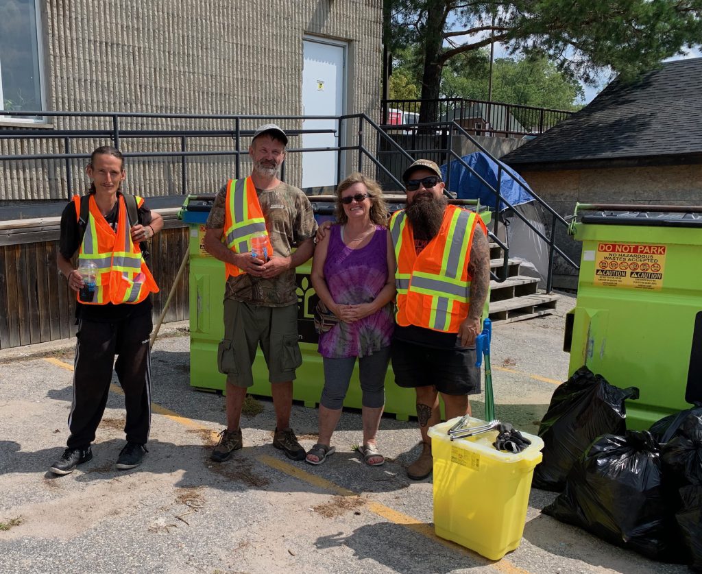 Three men in safety vests and one woman with garbage bags and ONLY paraphernaila