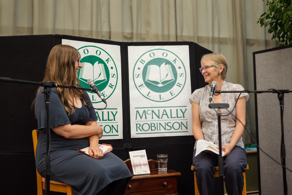 Angeline Schellenberg and Joanne epp are sitting on high stools behind microphones and in front of a sign that reads McNally Robinson Book sellers